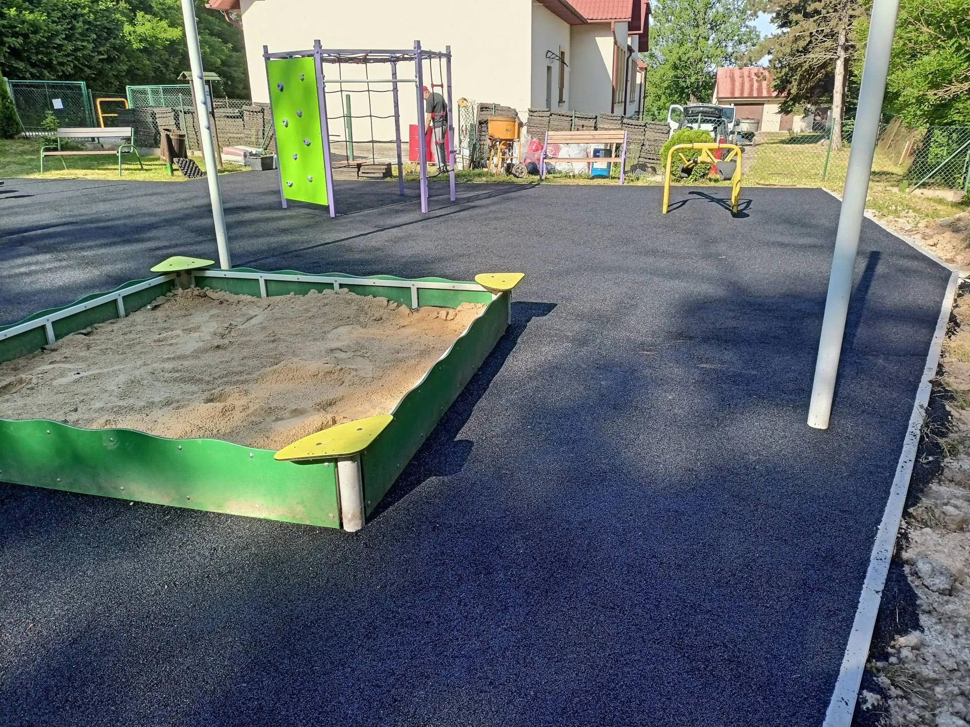 Plac zabaw z piaskownicą, urządzeniami i czarną nawierzchnią bezpieczną